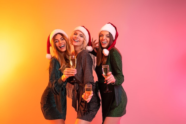 Trois filles heureuses dans des chapeaux de père noël tient des verres de champagne s'amusant à la fête du nouvel an