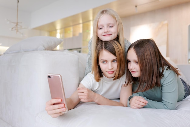 Trois filles sont allongées sur le canapé et regardent un téléphone.