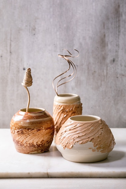 Trois formes différentes vases en céramique marron beige avec des fleurs sèches et des brindilles sur une table en marbre blanc avec un mur gris derrière. Copiez l'espace.