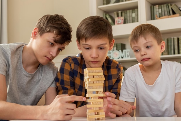 Trois frères garçons jouent à un jeu de société composé de blocs rectangulaires en bois tirant des pièces de