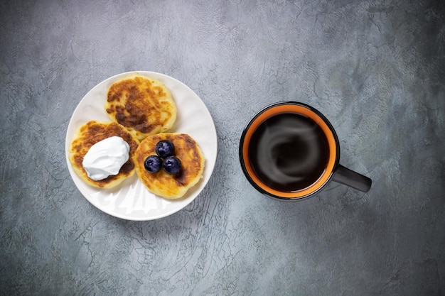 Trois gâteaux au fromage aux bleuets et crème sure sur plaque blanche blackorange tasse de café avec stea