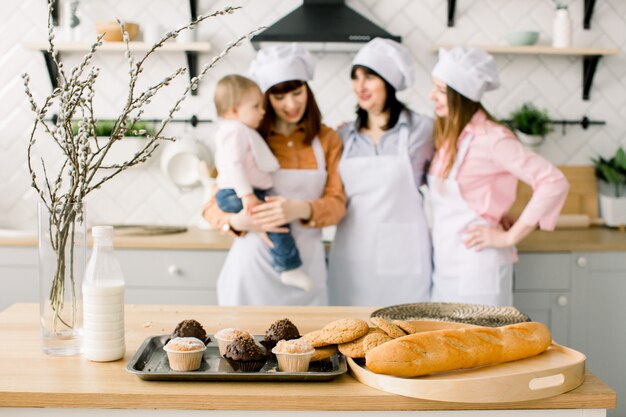 Trois générations de femmes cuisinent dans la cuisine, se concentrent sur la table avec des maffines et des biscuits. Nourriture maison et petite aide. Famille heureuse. Cuisson dans la cuisine. Vacances de Pâques ou fête des mères