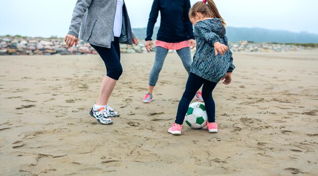 Trois générations de femmes jouant au football sur la plage en automne