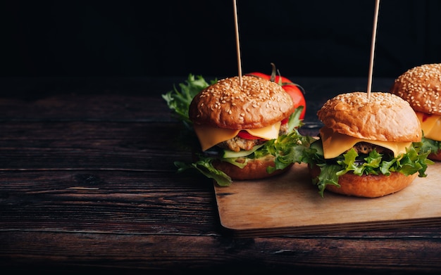 Trois hamburgers faits maison avec de la viande, du fromage, de la laitue, de la tomate sur une planche de bois sur une table