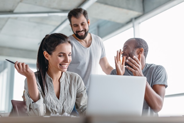 Trois hommes d'affaires divers se réjouissant ensemble sur un ordinateur portable tout en travaillant dans la salle de réunion du bureau. Équipe d'affaires travaillant sur leur projet d'entreprise ensemble au bureau. Notion de succès