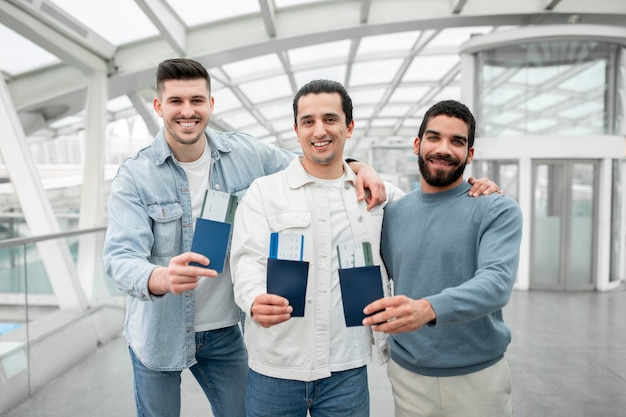 Trois hommes touristes montrant des cartes d'embarquement serrant debout dans l'aéroport