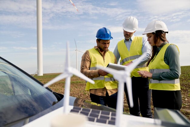 Trois ingénieurs debout sur le champ d'éolienne et discutant sur des modèles en plastique