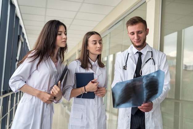 Trois internes en médecine à la recherche d'une image aux rayons X des poumons pour la pneumonie virale d'un patient Covid-19 en clinique Concept médical
