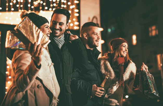 Trois jeunes couples joyeux s'amusant la nuit de Noël dans la rue de la ville avec beaucoup de lumières en arrière-plan.