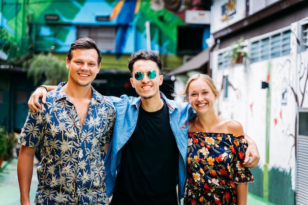 Trois jeunes d'ethnies différentes s'embrassant dans le dos au milieu d'une rue aux façades colorées ornées de street art