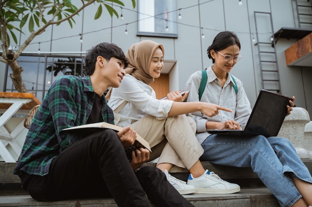 Trois jeunes étudiants asiatiques utilisant des ordinateurs portables assis sur des marches