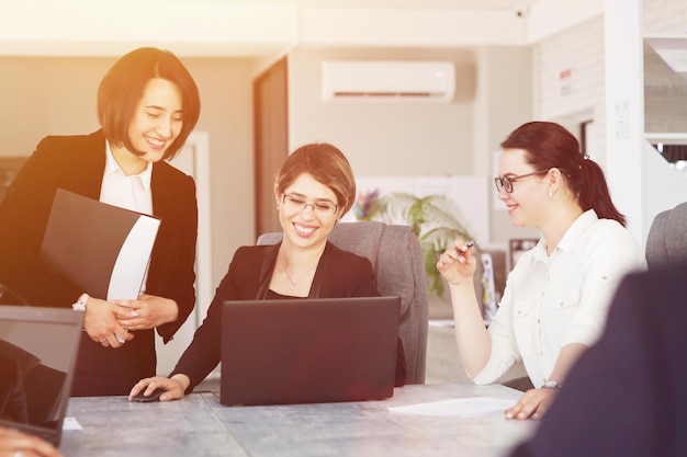 Photo trois jeunes femmes d'affaires prospères au bureau travaillent ensemble avec bonheur sur un projet