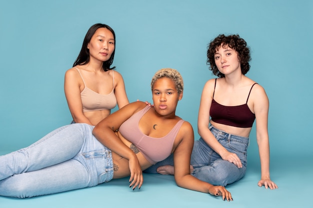 Trois jeunes femmes contemporaines reposantes d'ethnies asiatiques, caucasiennes et africaines se relaxant sur le sol sur fond bleu