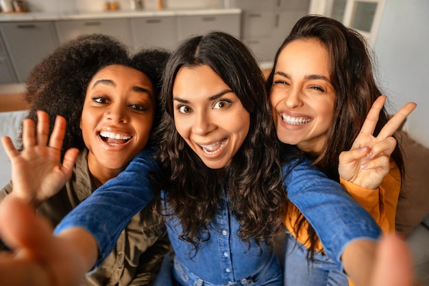 Trois jeunes femmes multiculturelles joyeuses prenant un selfie ludique à la maison