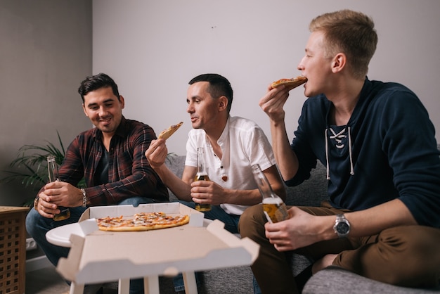 Trois jeunes gars gais mangeant de la pizza la prenant de la table