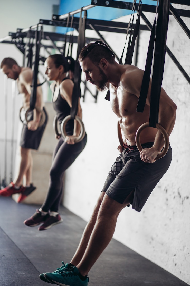 Photo trois jeunes hommes et femmes adultes faisant des tractions sur des anneaux