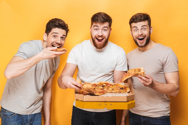 Trois jeunes hommes heureux mangeant une grosse pizza