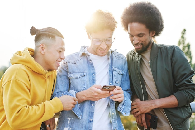 Photo trois jeunes hommes souriants debout et faisant défiler le téléphone portable