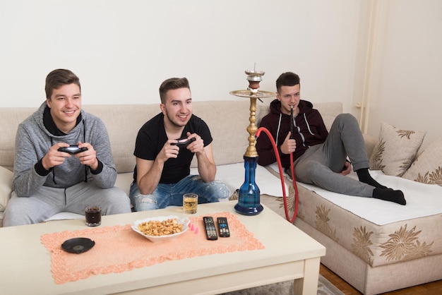 Trois jeunes joueurs assis ensemble sur un canapé et jouant à des jeux vidéo à la maison