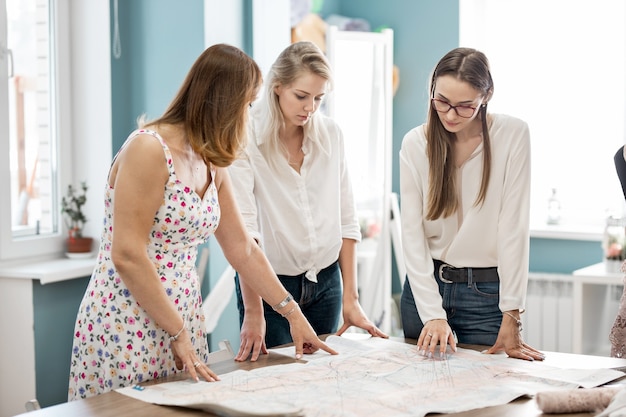 Trois jolies femmes élégantes pointent du doigt l'atelier des tailleurs de mode