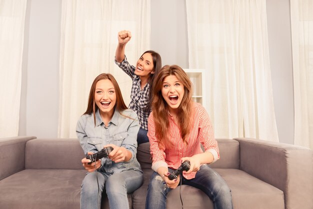 Trois jolies filles heureux assis sur un canapé et jouer à des jeux vidéo