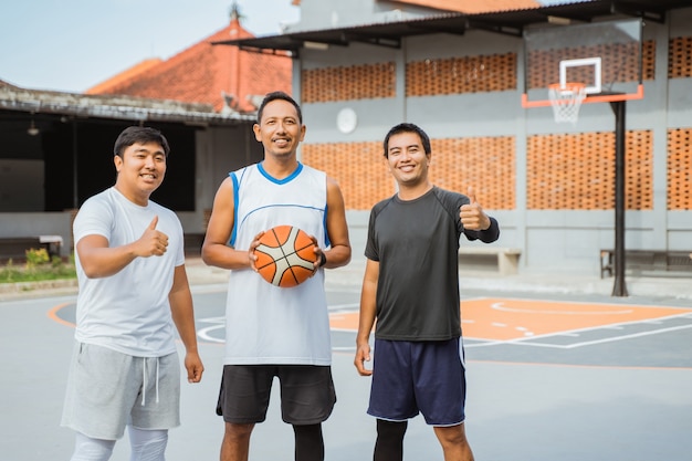 Trois joueurs de basket-ball souriant tout en portant le basket-ball et les pouces vers le haut