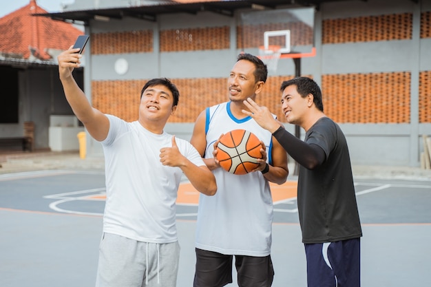 Trois joueurs de basket-ball souriant tout en prenant un selfie à l'aide d'un appareil photo de téléphone portable