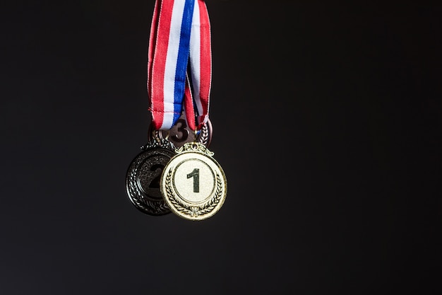 Trois médailles d'or, d'argent et de bronze accrochées sur un fond sombre. Concept de sport et de victoire.