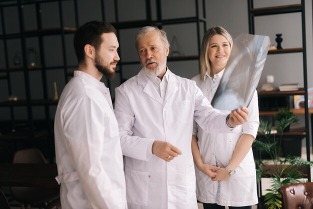 Trois médecins adultes et jeunes examinant une radiographie ensemble dans la salle de consultation. Les médecins discutent de la poursuite du traitement du patient tel que prescrit par le médecin. Concept de travail médical d'équipe.