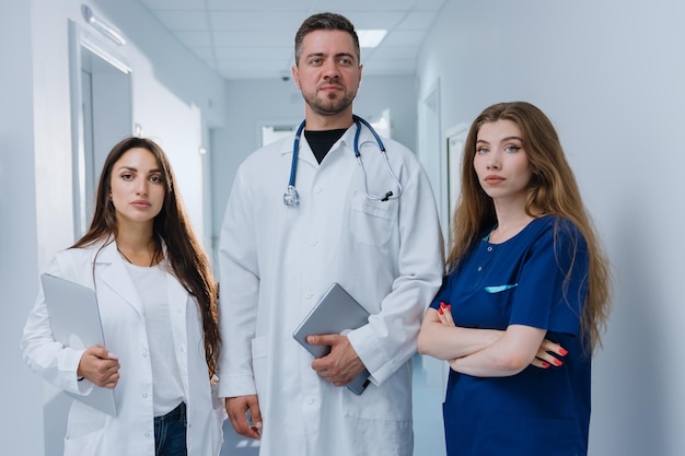 Trois médecins professionnels se tiennent dans le couloir de la clinique et regardent la caméra Mise au point sélective sur le médecin de sexe masculin