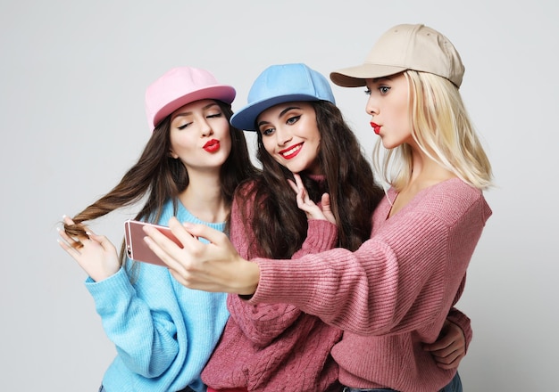 Trois meilleures copines heureuses portant des chandails et des casquettes faisant selfie sur smartphone