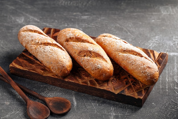 Trois miches de baguette fraîchement cuite sur la planche à découper en bois sur fond gris