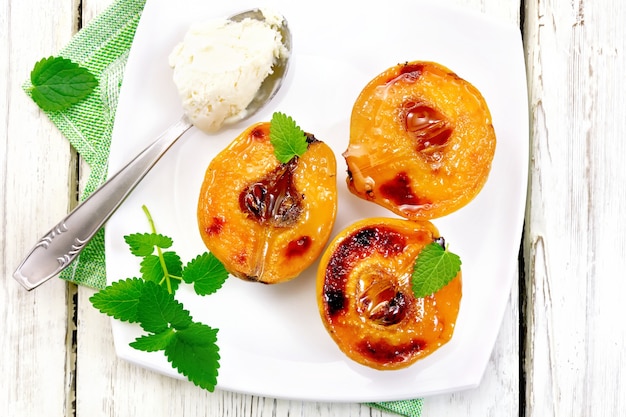 Trois moitiés de coings cuits avec du miel, de la menthe et une cuillère avec de la crème glacée dans une assiette sur une serviette sur un fond de planche de bois sur le dessus