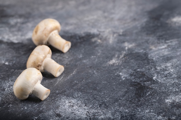 Trois morceaux de champignons crus placés sur une surface en marbre.