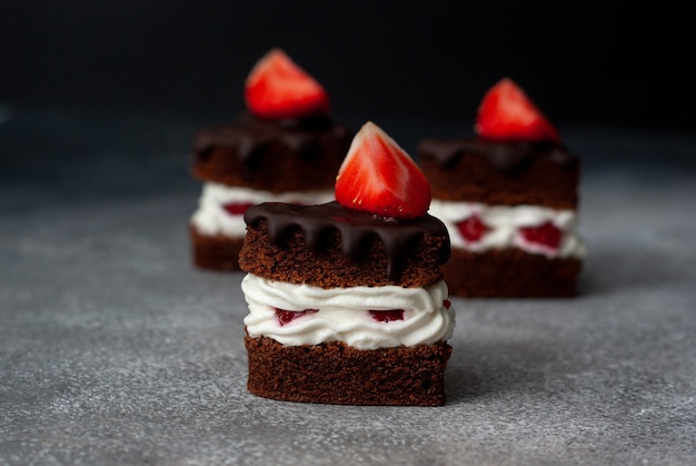 Trois morceaux de gâteau en couches aux fraises au chocolat avec de la crème blanche sur fond gris foncé