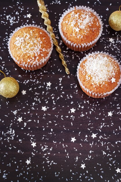 Trois muffins orange faits maison décorent la poudre de noix de coco sur du bois foncé