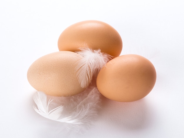 Photo trois œufs sur fond blanc avec des plumes