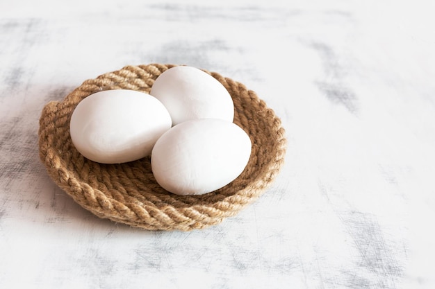 Trois oeufs de Pâques blancs posés sur un plateau en ficelle fond vintage en bois blanc