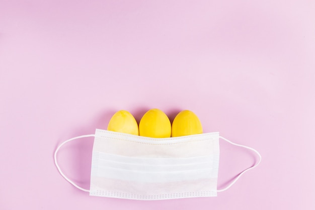 Photo trois oeufs de pâques de couleur jaune avec un masque protecteur sur fond rose