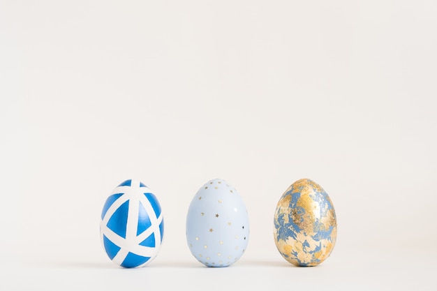 Trois oeufs de Pâques décorés d'or sur une surface bleue. Concept de Pâques minimal.