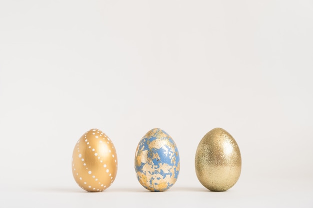 Trois oeufs de Pâques décorés d'or sur une surface bleue. Concept de Pâques minimal.