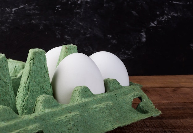 Trois œufs de poule blancs dans un récipient vert sur une table en bois marron.