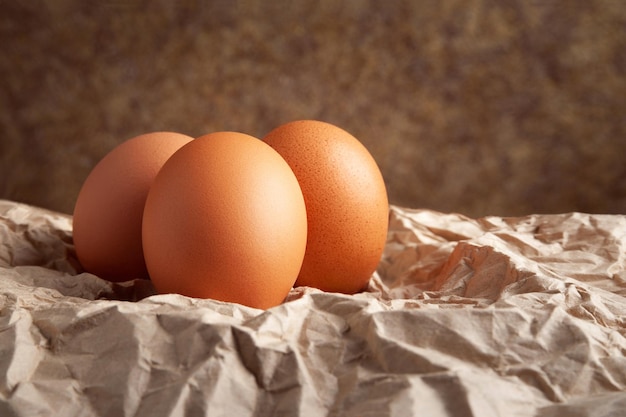 Photo trois œufs de poule oeufs de poule bruns crus sur du papier d'emballage froissé sur fond sombre