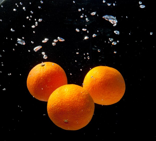 Trois oranges dans de l'eau avec des bulles