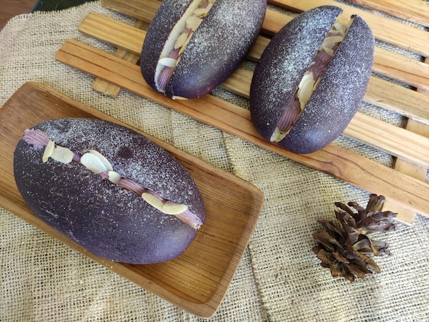 Trois pains violets sur un plateau en bois avec une pomme de pin sur le côté.