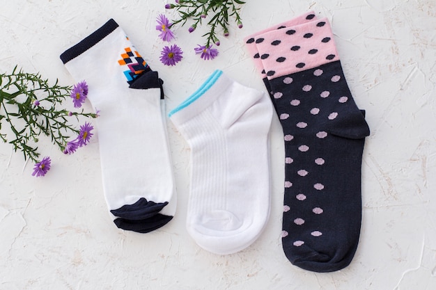 Trois paires de chaussettes pour femmes et fleurs sur fond blanc structuré, vue de dessus.