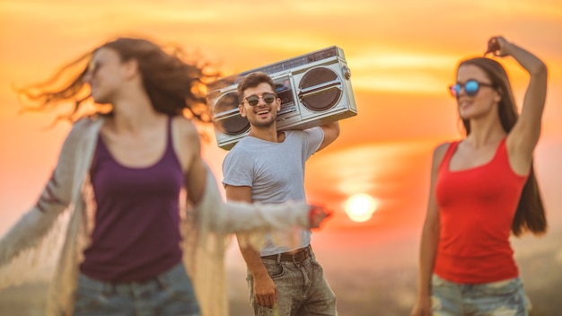 Les trois personnes avec un boom box dansant sur fond de coucher de soleil