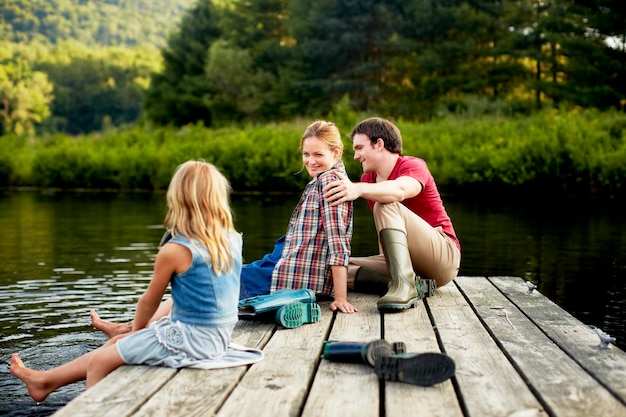 Trois personnes, deux adultes et un enfant se reposant sur un ponton, les pieds dans l'eau.