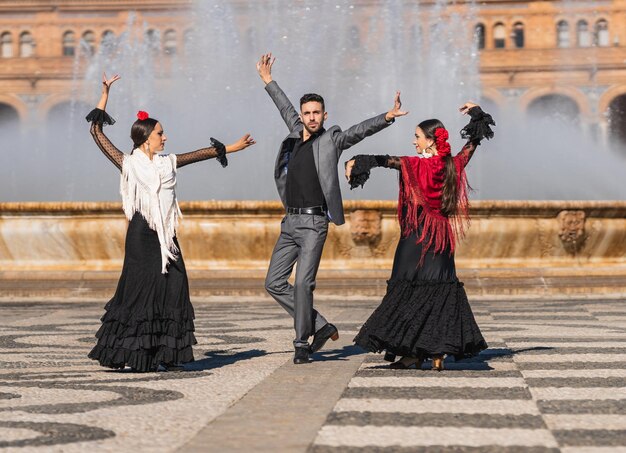 Photo trois personnes avec tenue de flamenco dansant sur la place traditionnelle d'espagne à séville