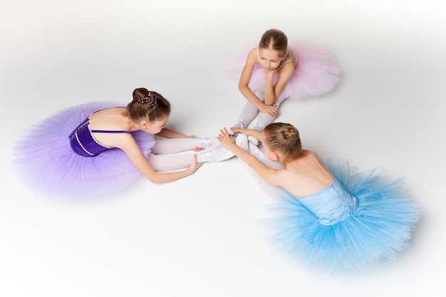Trois petites filles de ballet assises en tutu multicolore et chaussons de pointe ensemble sur fond blanc
